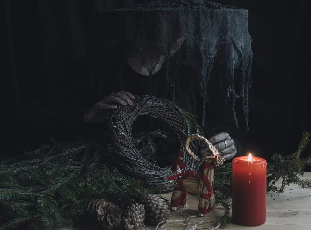 Some traditional Yule items. A woman holding a wreath next to a lit candle.