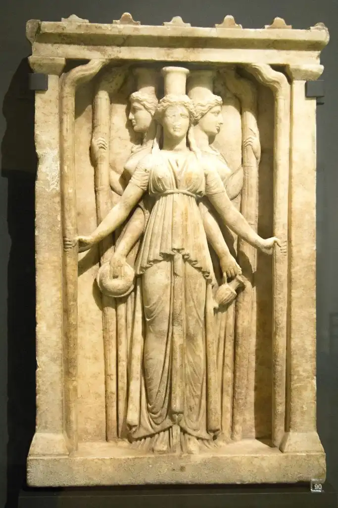 Relief of triplicate Hekate. Three female figures framed in aedicula, with high poloi on their heads, dressed in chiton and peplos, holding torches in their hands.